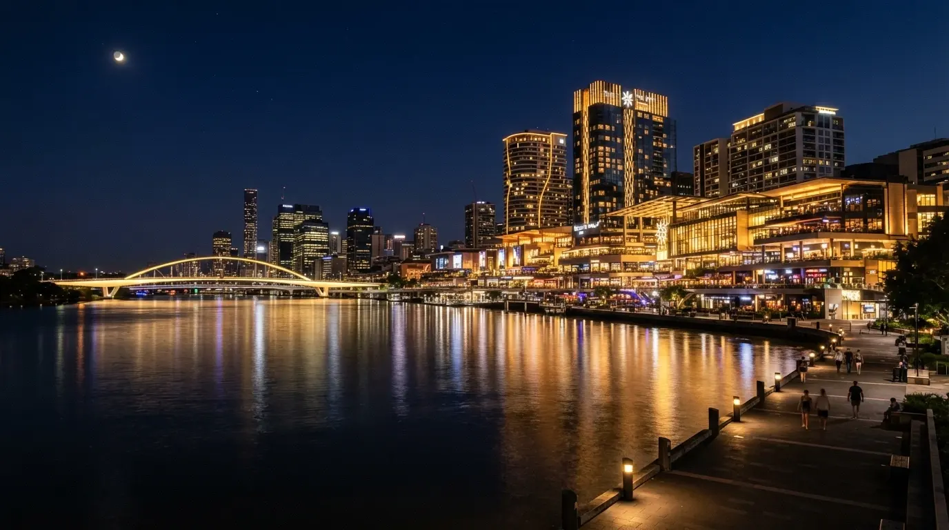 Night view of the Queen's Wharf precinct lit up along the Brisbane River, with the city skyline behind