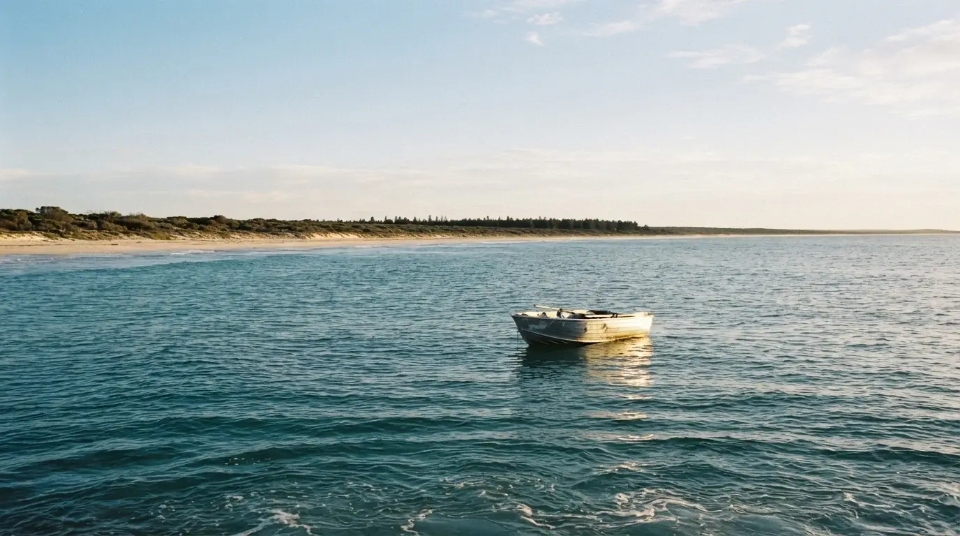 An Australian shoreline seen from the water looking back at the coast, with a small boat in the foreground and the land distant — no people, no text, purely atmospheric